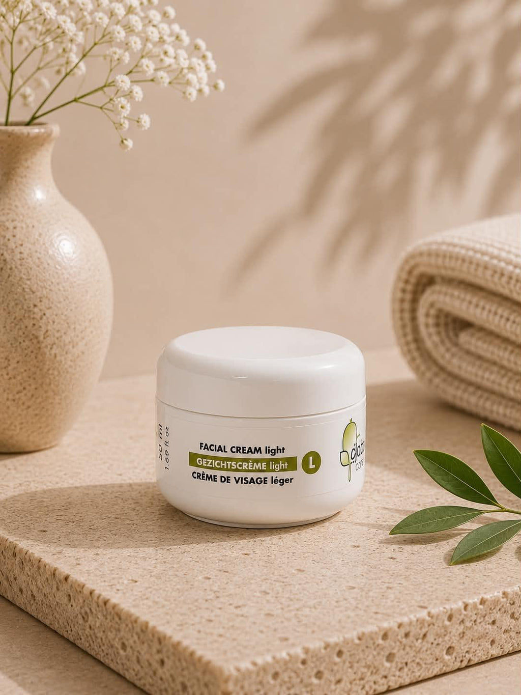 Crème de visage légère Jojoba Care dans un pot blanc sur un socle en pierre naturelle.