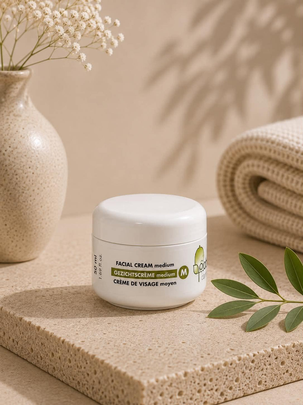 Crème de visage moyenne Jojoba Care dans un pot blanc sur un socle en pierre naturelle.