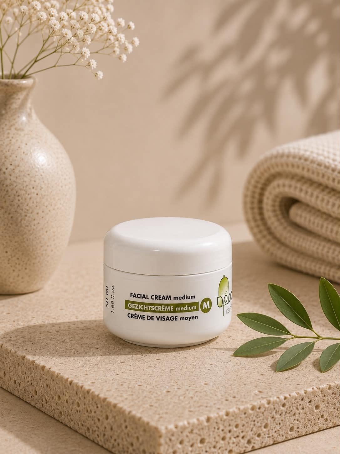 Crème de visage moyenne Jojoba Care dans un pot blanc sur un socle en pierre naturelle.
